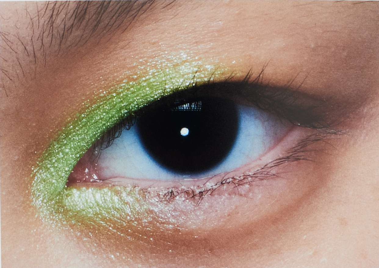 Close-up of a human eye featuring vibrant green eyeshadow, highlighting beauty and cosmetic artistry in a studio setting.