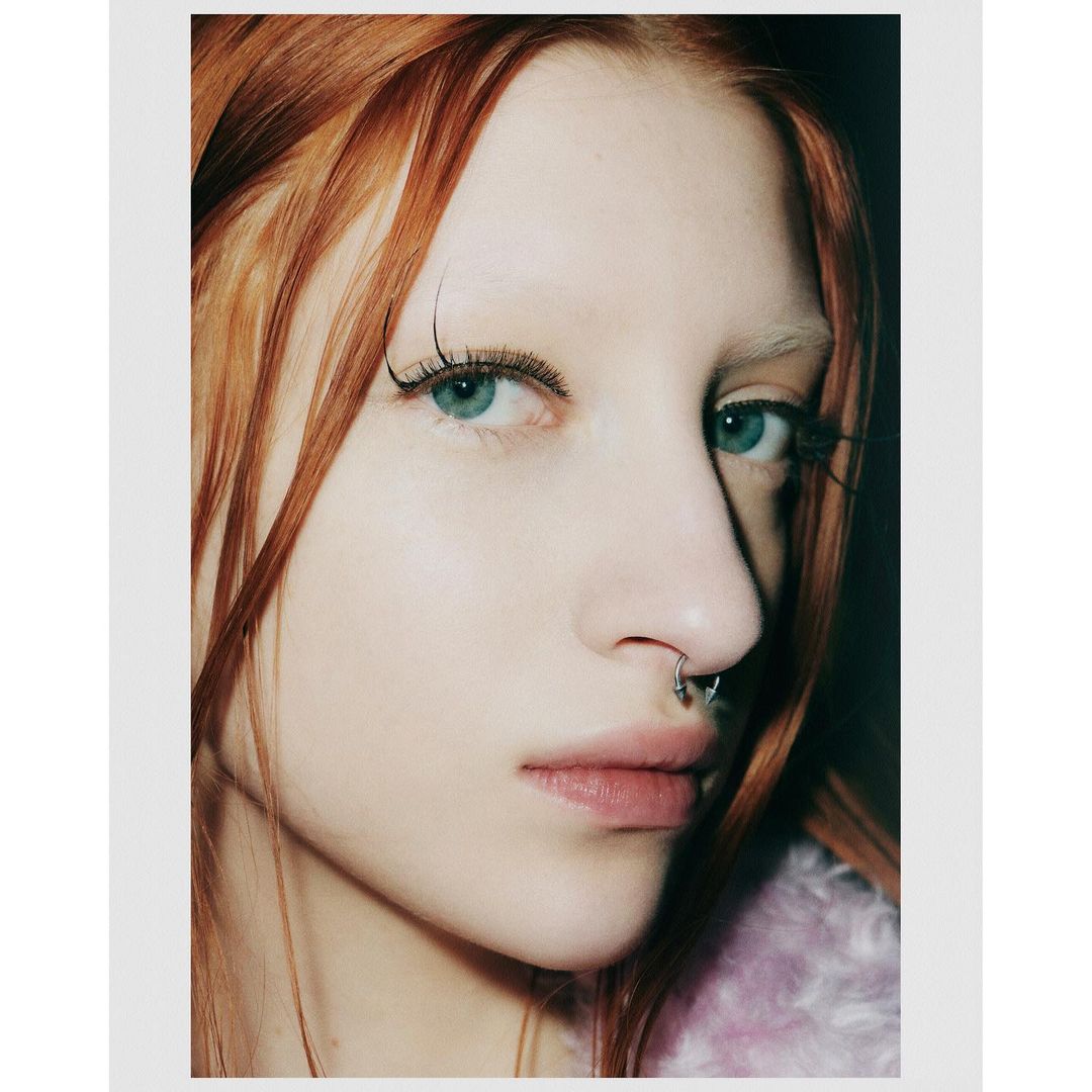 Close-up studio portrait of an adult woman with red hair, light skin, and a septum piercing, showcasing beauty and fashion.