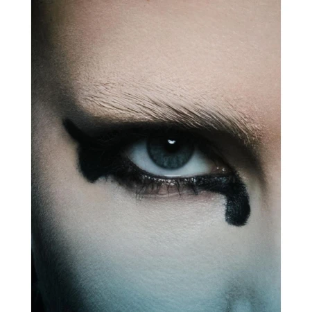 Close-up portrait of a person with dramatic black eyeliner, pale eyebrows, and a blue eye photographed by Andrew Vowles