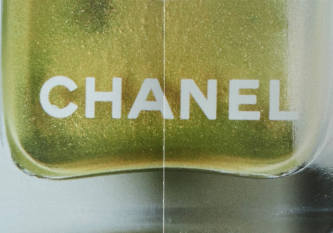 Close-up of a 'Chanel' nail polish bottle revealing shimmery, golden-green polish inside, with a shallow depth of field and beauty focus.