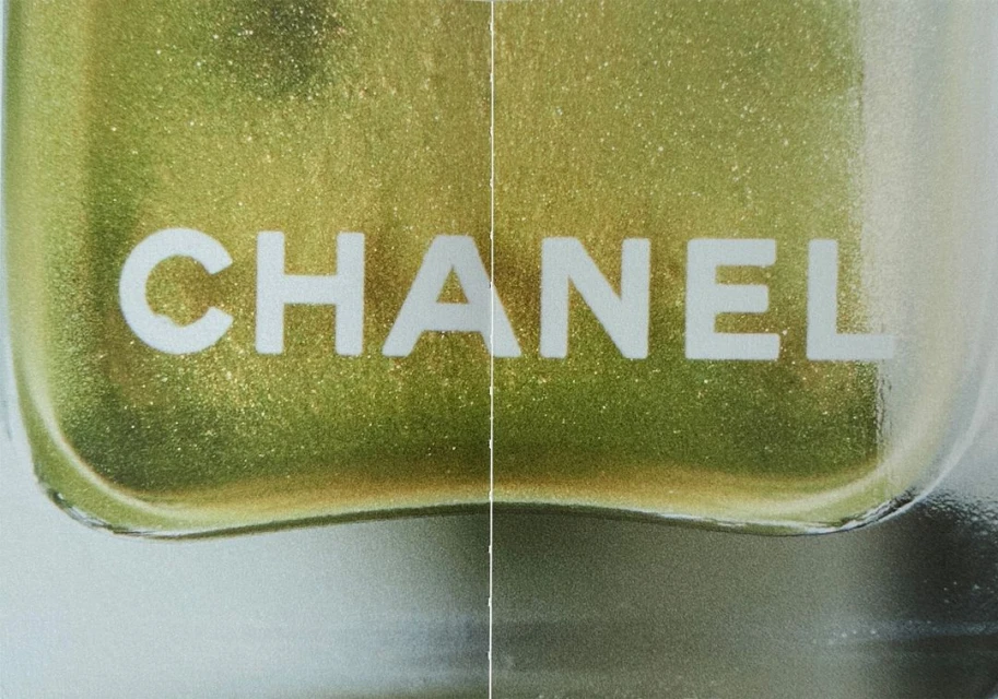 Close-up of a 'Chanel' nail polish bottle revealing shimmery, golden-green polish inside, with a shallow depth of field and beauty focus.