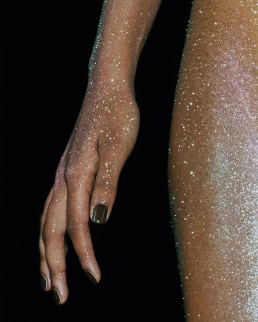Closeup of an adult arm and body covered in fine glitter against a solid black background, showcasing texture and artistic body painting.