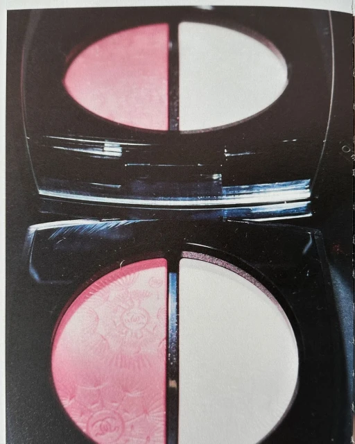 Close-up of a black makeup compact featuring a half-and-half blush and powder with pink and white tones, in indoor lighting.