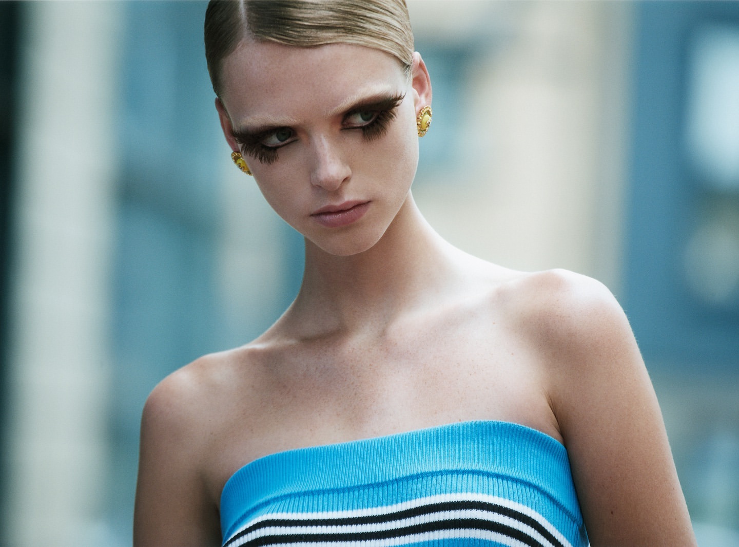 Close-up of a woman with large eyelashes wearing a striped top against a blurred background. Fashion and beauty shot. 