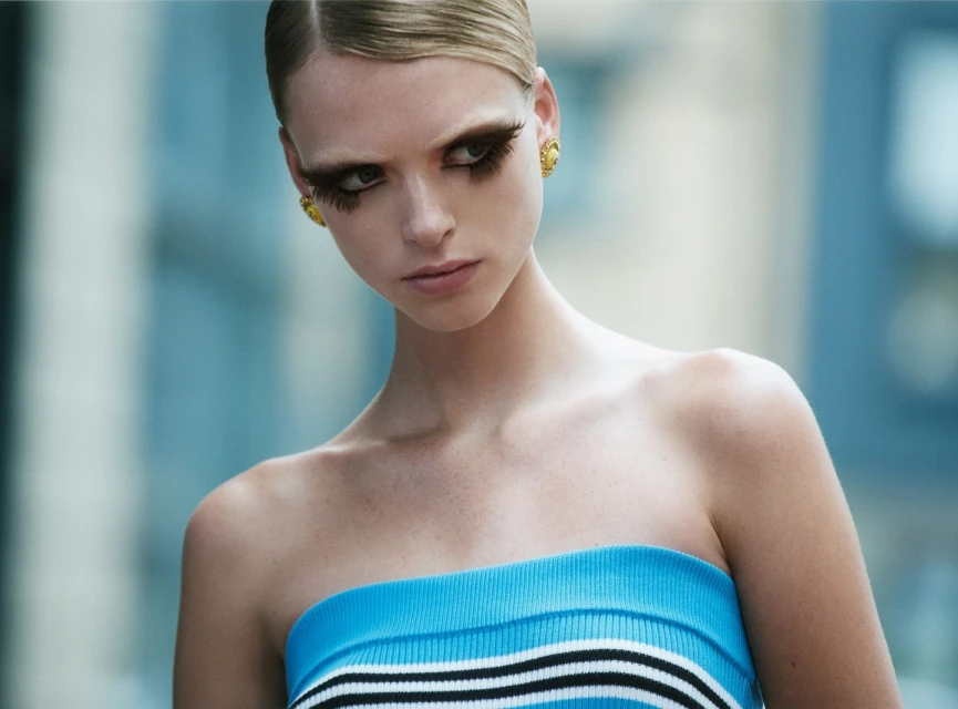Close-up of a woman with large eyelashes wearing a striped top against a blurred background. Fashion and beauty shot. 