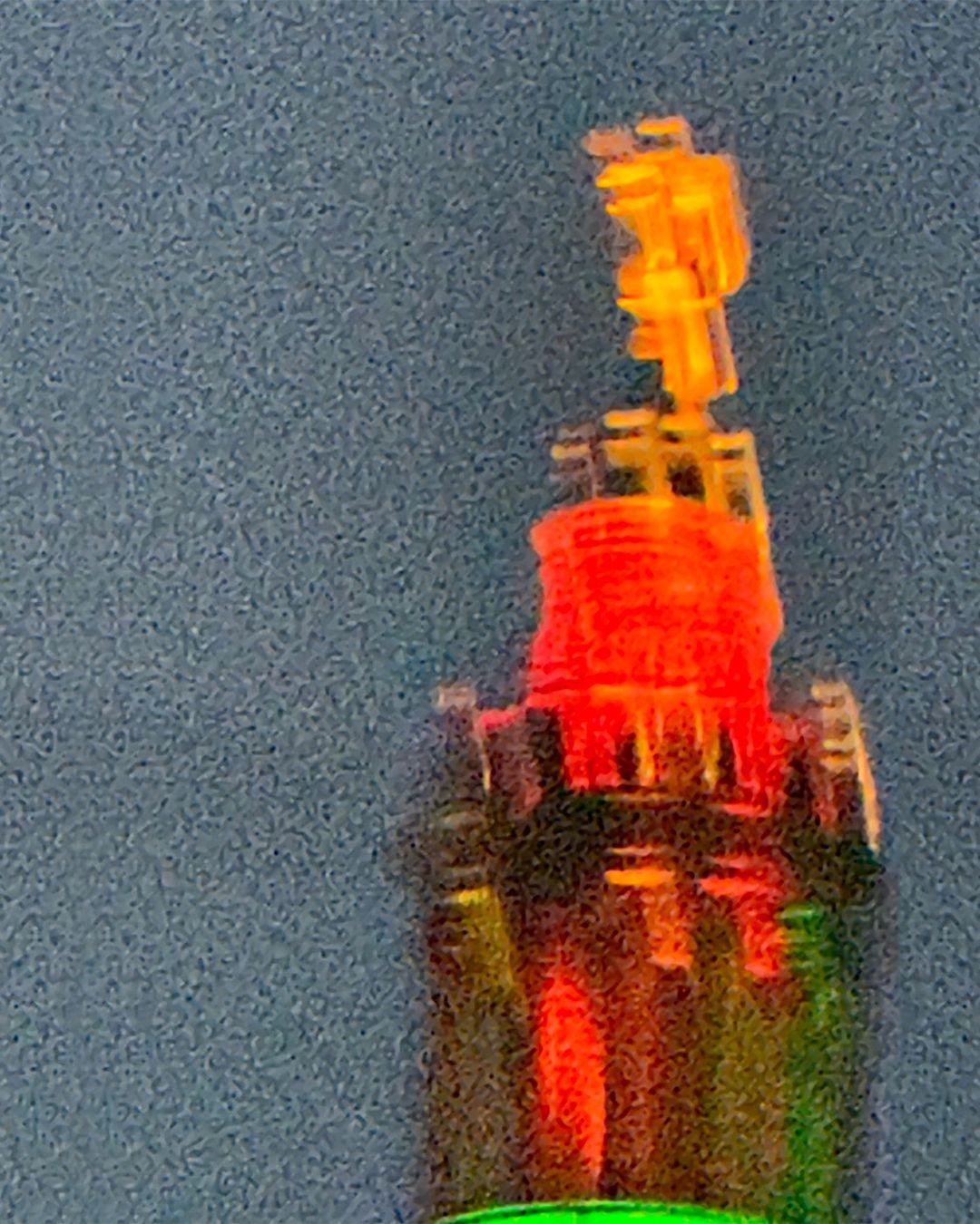 Close-up of a colorful, blurred, abstract object against a dark background. The object features a tower-like structure with red and yellow hues.