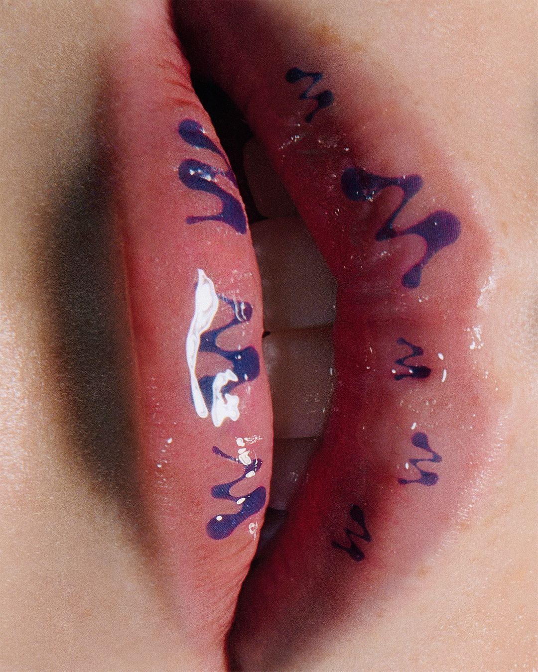 Close-up of painted lips with glossy finish. Dark blue and white abstract designs decorate the skin around the mouth.