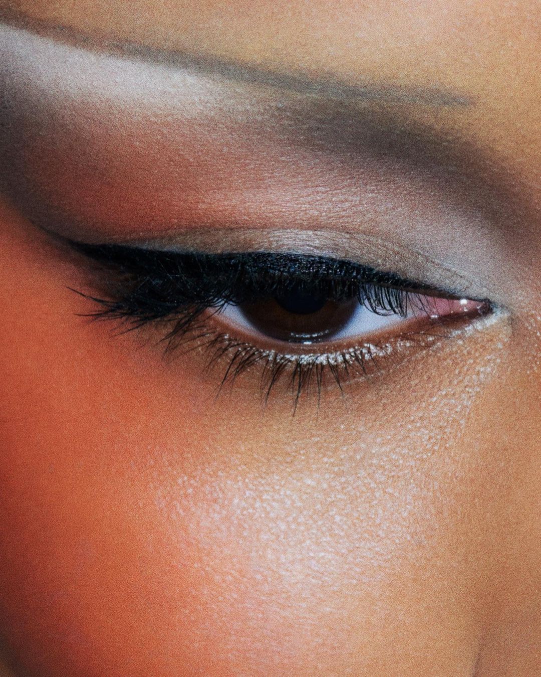 Close-up portrait of a woman's eye with black eyeliner and subtle eyeshadow, highlighting the details of her skin and makeup.