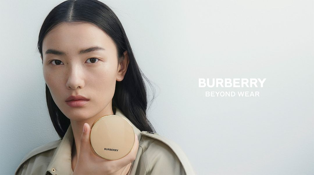 Asian model poses with Burberry compact in a studio shot, promoting beauty and fashion. Focus on face, minimal makeup, and clean background.