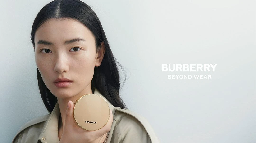 Asian model poses with Burberry compact in a studio shot, promoting beauty and fashion. Focus on face, minimal makeup, and clean background.