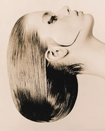 Profile portrait of a woman with slicked-back dark hair and dramatic winged eyeliner against a plain sepia background