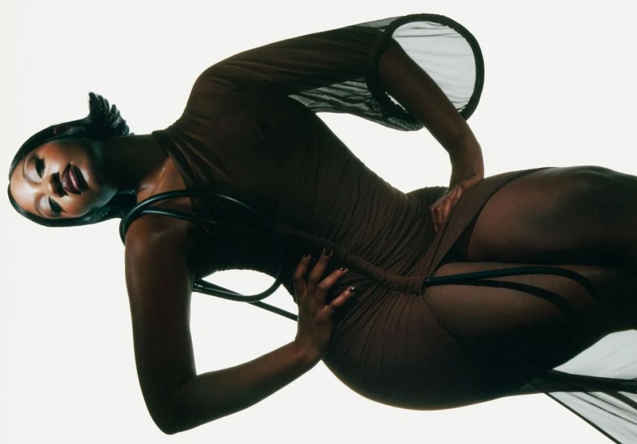 Attractive Black woman posing in sheer brown dress in studio. Fashion shot, beauty and style, sensual expression, indoor environment.