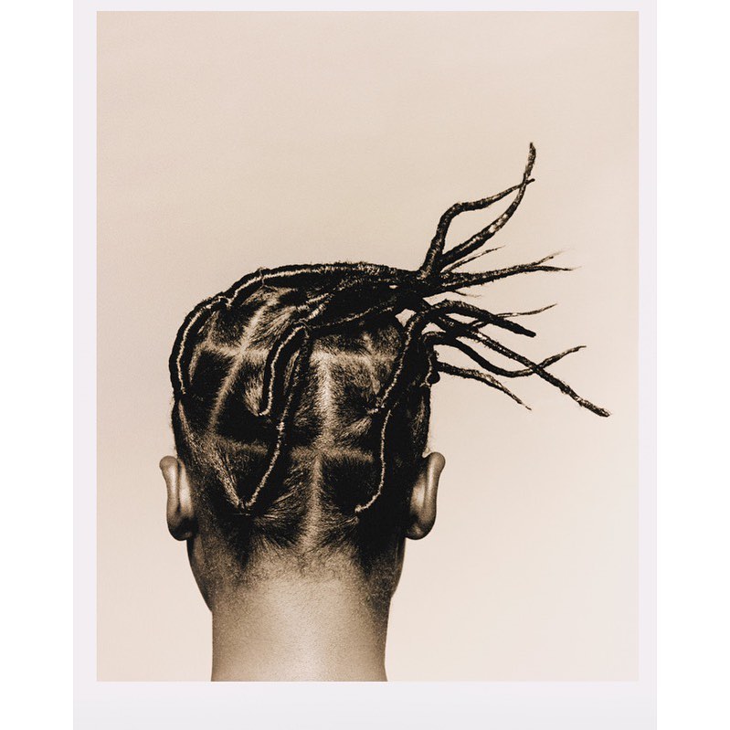 Close-up studio portrait of a man with unique braided hair design on a neutral backdrop showcasing hairstyle, neck, and ears.