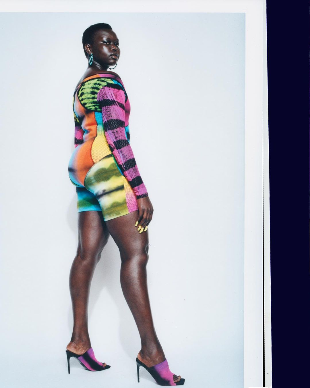Fashionable Black woman with short hair poses in colorful top and shorts with matching heels in a studio shot against a white background.