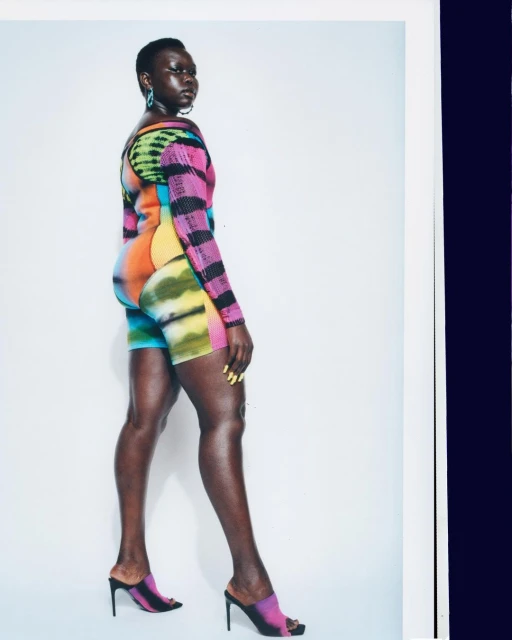 Fashionable Black woman with short hair poses in colorful top and shorts with matching heels in a studio shot against a white background.