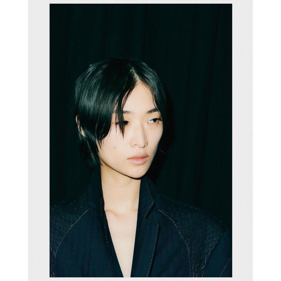 Portrait of a short-haired woman in a dark blazer against a dark curtain backdrop photographed by Andrew Vowles.