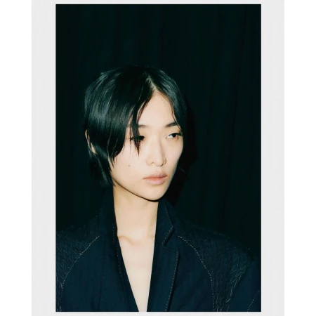 Portrait of a short-haired woman in a dark blazer against a dark curtain backdrop photographed by Andrew Vowles.