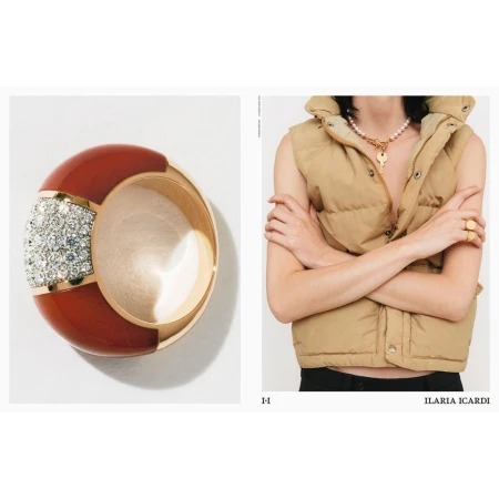 Still life shot of a red and gold ring with gemstones next to a person wearing a puffer vest and necklace with a key pendant.