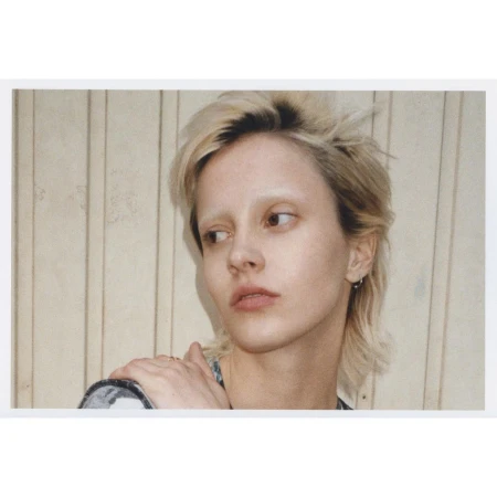 Close-up portrait of a person with bleached blonde mullet hair and light brows against vertical wooden panels