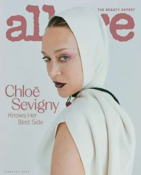 Chloe Sevigny wearing a cream hooded top with a cherry necklace against a light grey background