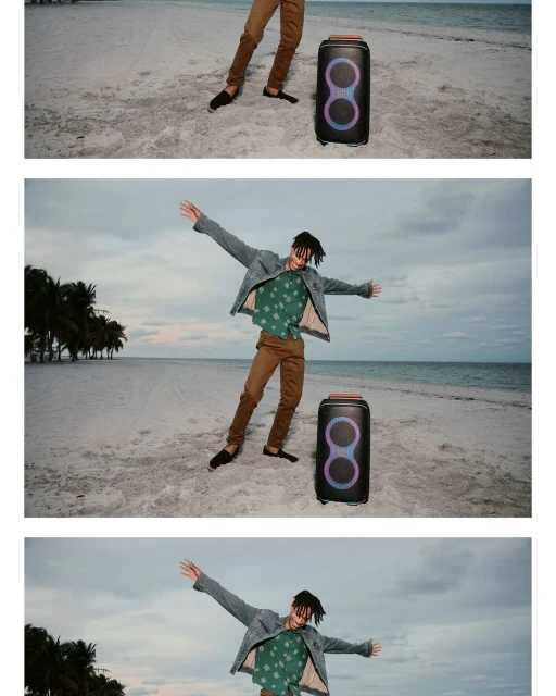 Man with open arms stands on a sandy beach next to a large portable speaker with palm trees and ocean in the background.