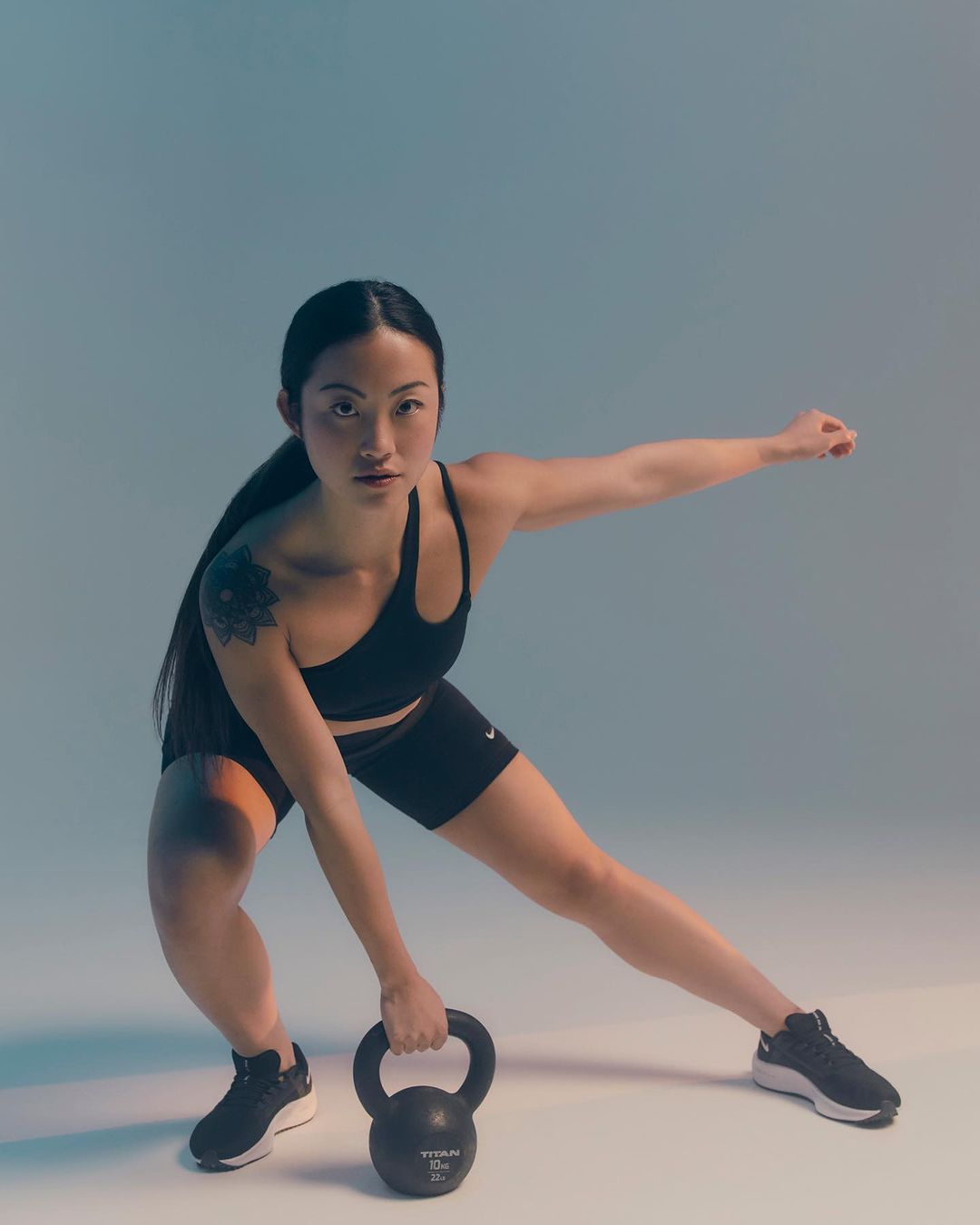 Athletic woman in fitness attire holding a kettlebell while exercising in a brightly lit studio, wearing Nike activewear.