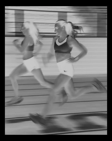 Two female runners in athletic wear captured mid-stride in motion blur on a track, photographed by Andrew White.