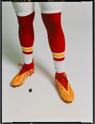 Close-up of a person wearing red and yellow striped athletic socks and orange cleats against a white background