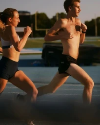 Two runners running on an outdoor running track during golden hour lighting