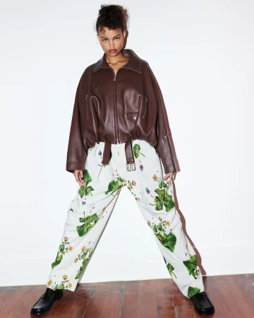 A model poses in a brown leather jacket and floral pants in a bright studio, offering a modern, edgy fashion statement.