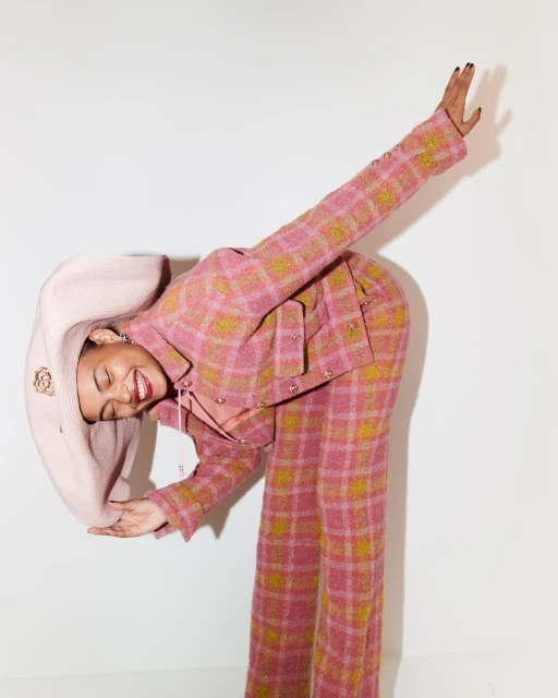 Woman in a pink plaid suit and matching hat posing with a smile in a bright studio setting, fashion forward and expressive.