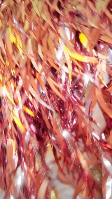 Abstract view of metallic tinsel in red, copper, and gold shades, creating a shimmering and textured visual effect with blurred background.