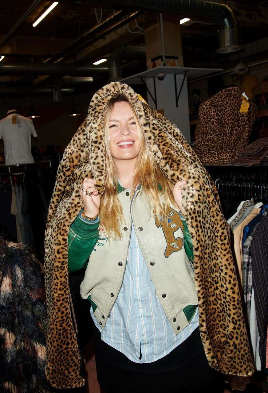 Smiling woman draped in a leopard print coat in a vintage clothing store, posing for fashion editorial photography.