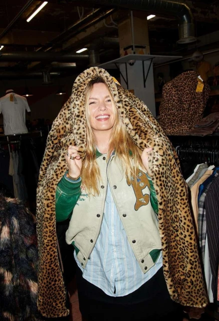 Smiling woman draped in a leopard print coat in a vintage clothing store, posing for fashion editorial photography.