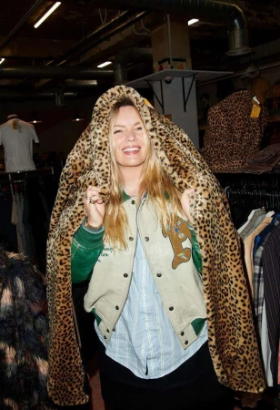 Smiling woman draped in a leopard print coat in a vintage clothing store, posing for fashion editorial photography.