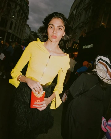 A young woman in a yellow top eats French fries in a city street scene, with a McDonald's restaurant sign visible in the background.