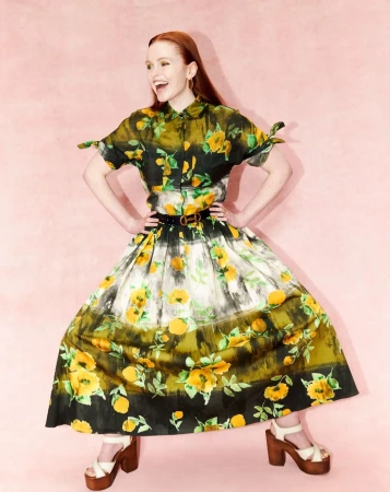 Red-haired woman in a floral print shirt and midi skirt posing against a textured pink background by Andrew Woffinden