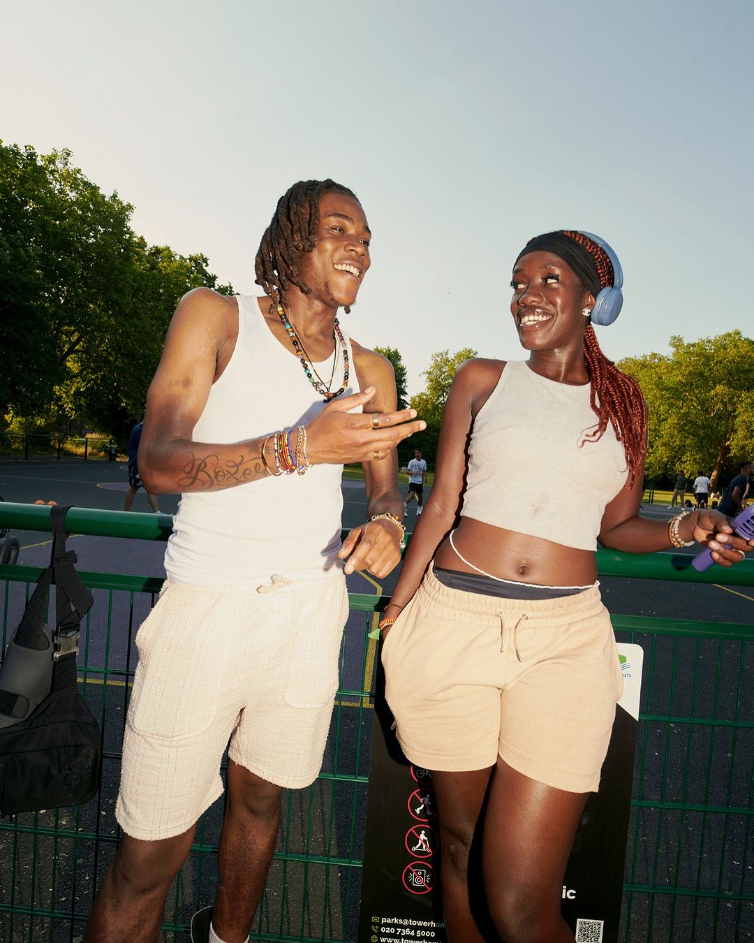 Two adults enjoy a sunny day in a park, smiling at each other while dressed in tank tops and casual shorts in an outdoor setting.