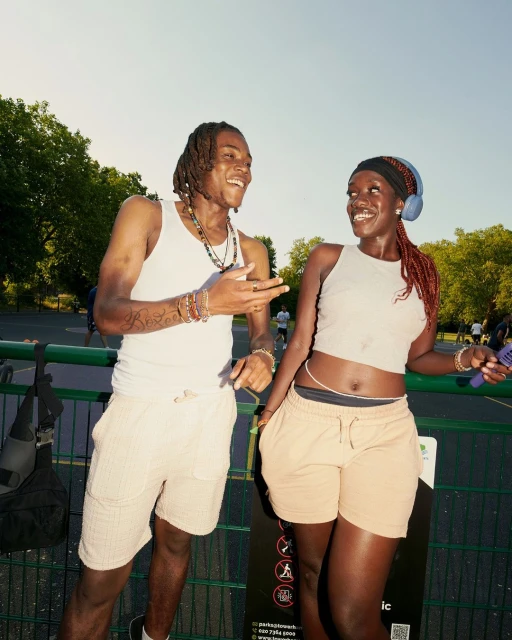 Two adults enjoy a sunny day in a park, smiling at each other while dressed in tank tops and casual shorts in an outdoor setting.