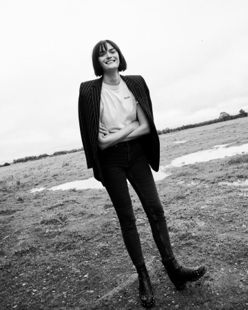 Monochrome portrait of a smiling woman with dark bobbed hair wearing a pinstripe blazer outdoors in a field