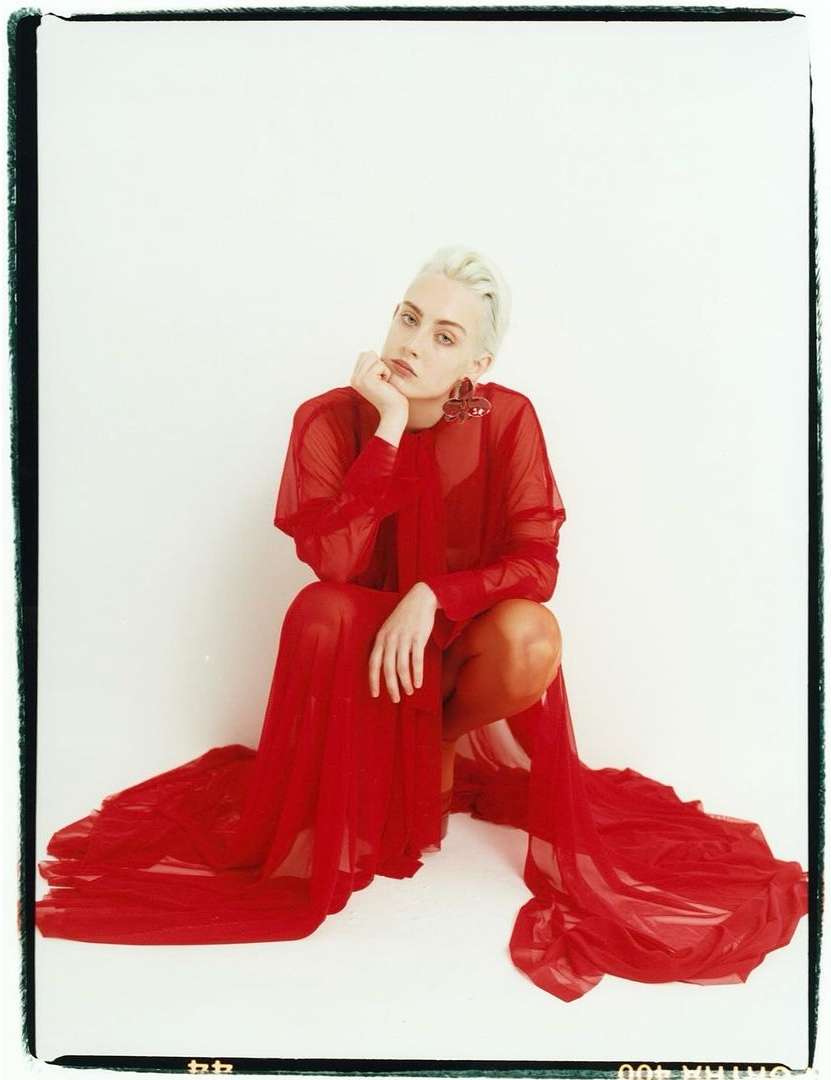 Woman with short blonde hair poses in a sheer red dress against a white background in a studio portrait. Fashion and beauty.
