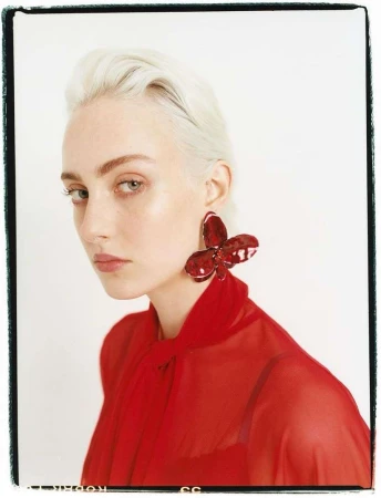 Portrait of a white woman with short platinum blonde hair wearing a red blouse and large red butterfly earring.