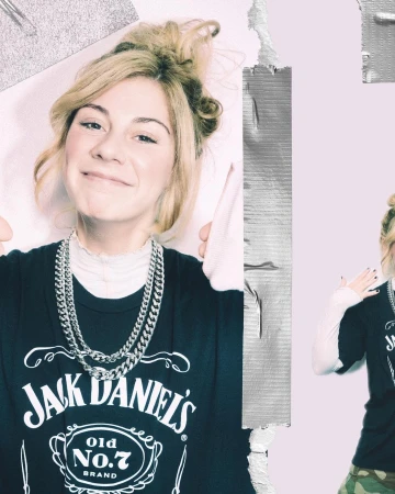Smiling woman wearing a Jack Daniel's t-shirt and silver chains poses in a studio with tape and a felt board for a trendy aesthetic.