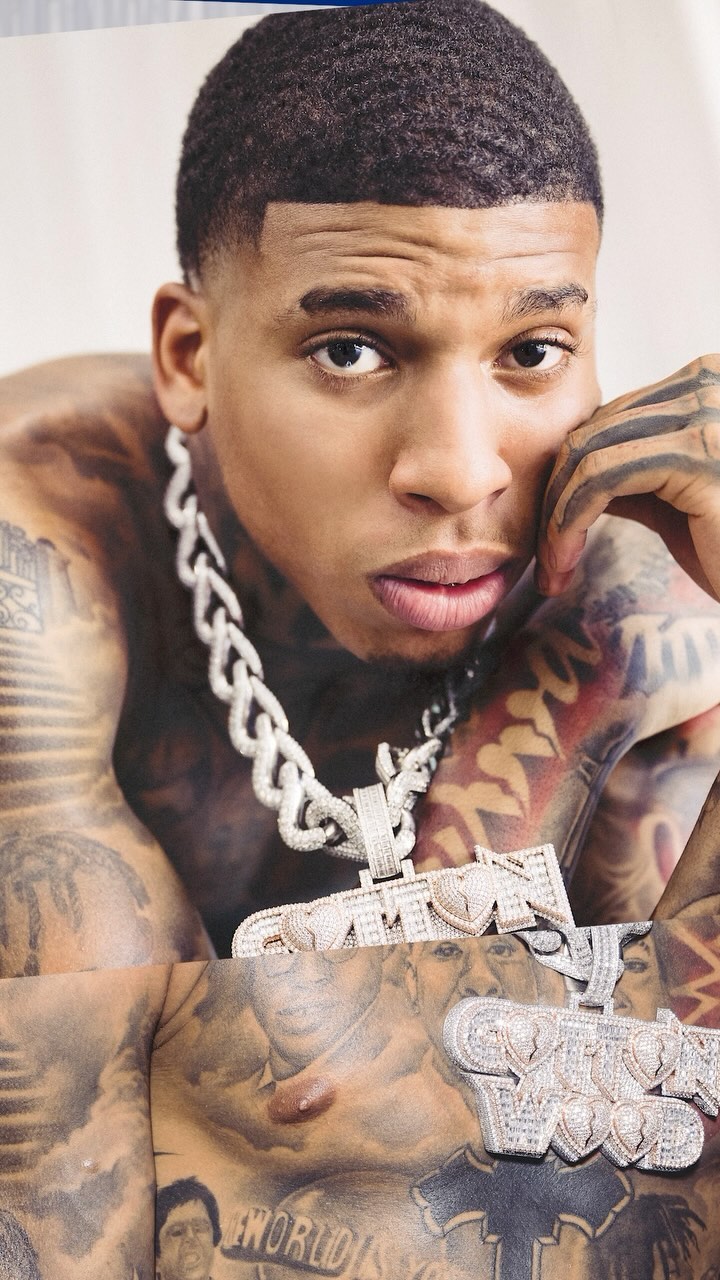 Close-up portrait of a shirtless adult male with tattoos and a silver chain necklace, posing indoors with an intense facial expression.