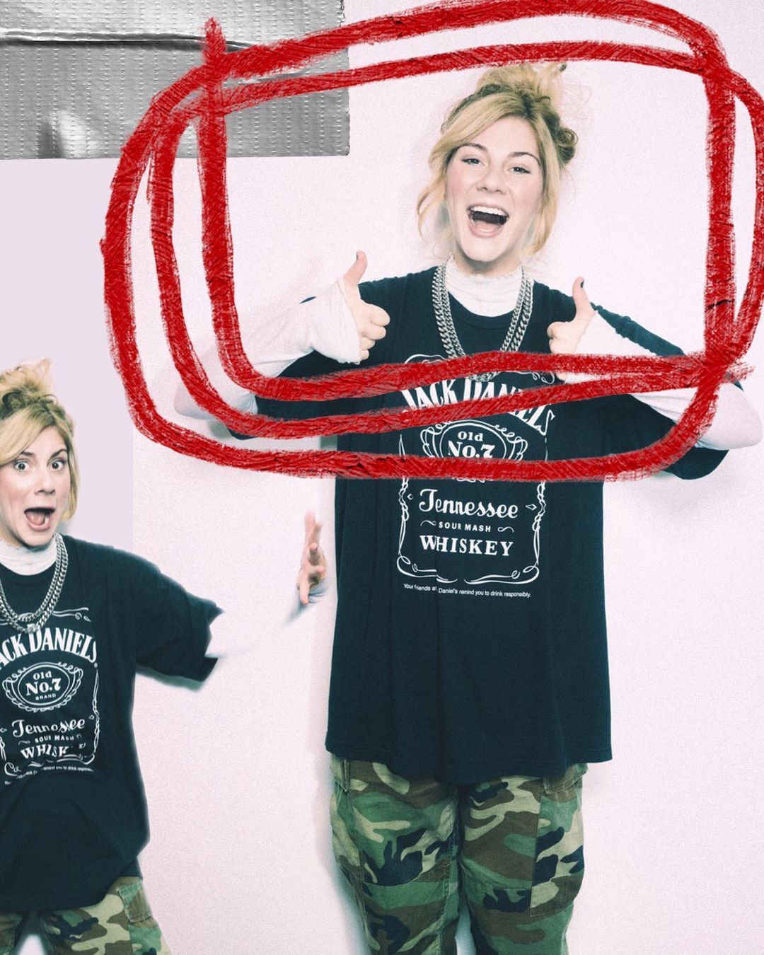 A young blonde woman smiles, wears a Jack Daniel's t-shirt and camo pants, and gives two thumbs up in a bright, indoor setting.