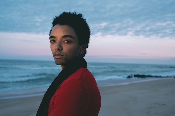 Portrait of a young man wearing a red shirt and black scarf against an ocean beach at dusk by photographer Andrew Zaeh