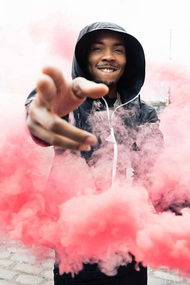 Smiling man with hand outstretched and pink smoke. Portrait of a person in a hooded jacket in front of pink smoke.