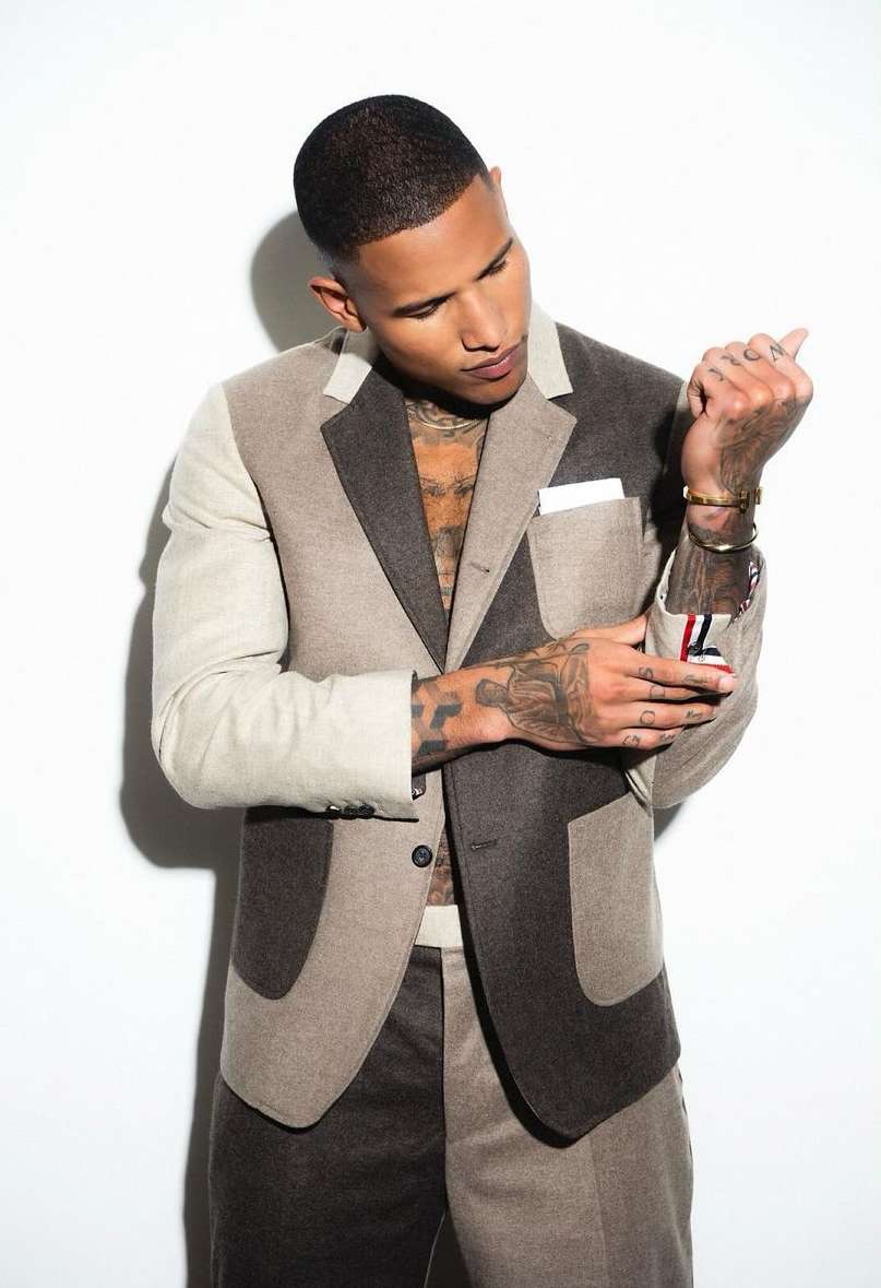 Man in a modern color-blocked suit poses against a white background, showcasing its unique design and tailored fit with chest and arm tattoos.