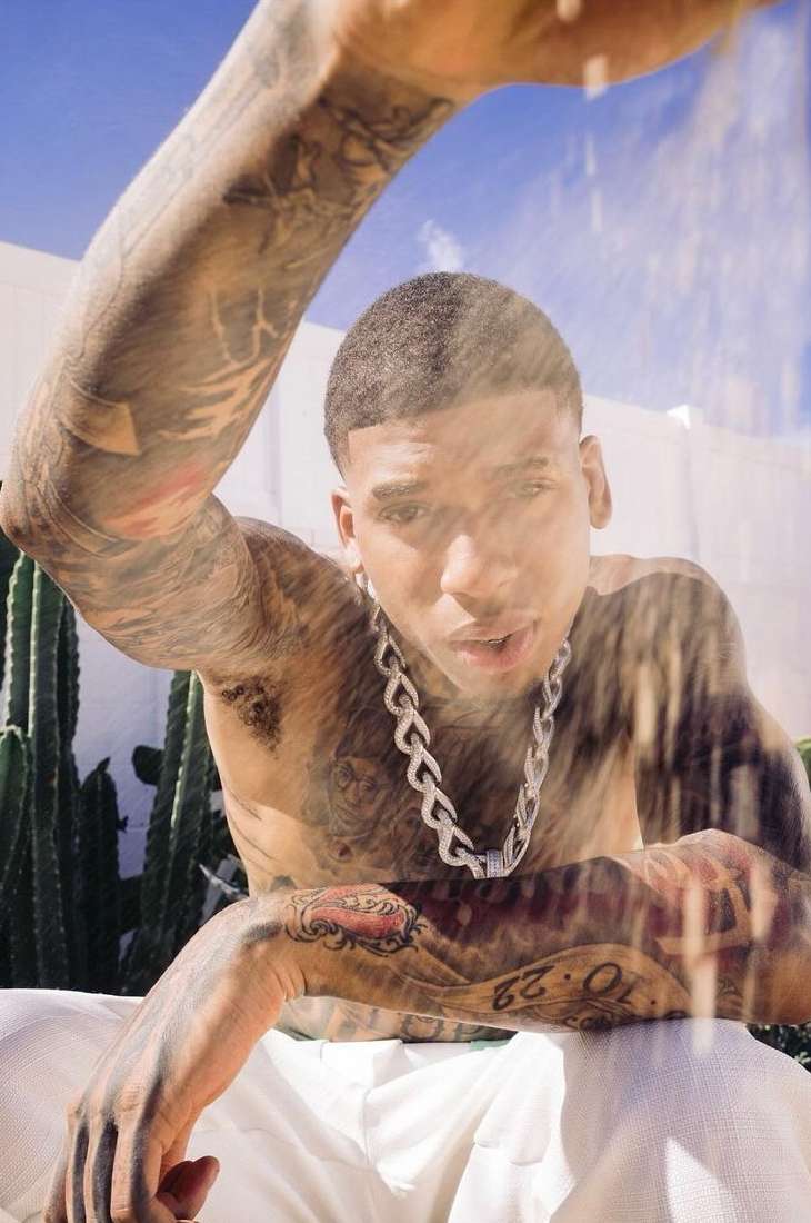 Shirtless man with extensive arm tattoos wearing a chunky silver chain necklace outdoors near cacti.