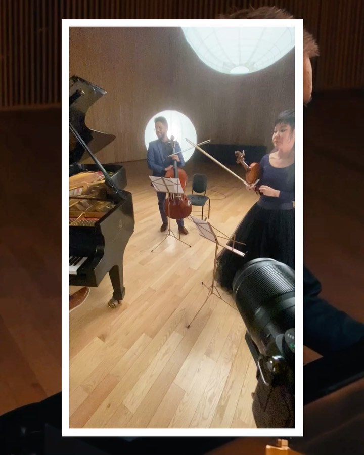 Indoor performance featuring three musicians: a pianist, a cellist and a violinist performing on stage in front of a circular light.